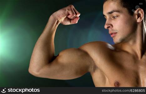 sport, bodybuilding, strength and people concept - close up of young man flexing and showing biceps over dark background