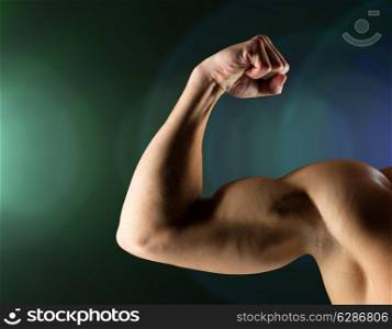 sport, bodybuilding, strength and people concept - close up of young man flexing and showing biceps over dark background