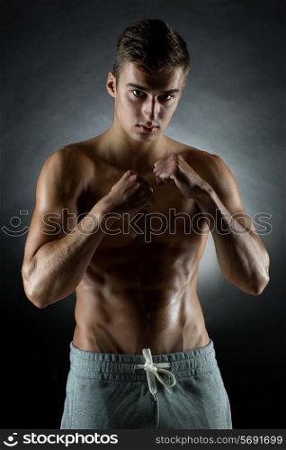 sport, bodybuilding, strength and people concept - young man in fighting stand over black background