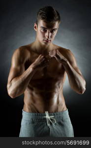 sport, bodybuilding, strength and people concept - young man in fighting stand over black background