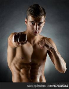 sport, bodybuilding, strength and people concept - young man in fighting stand over black background