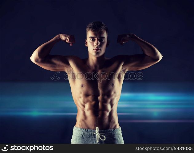 sport, bodybuilding, strength and people concept - young man showing biceps and muscles over dark background