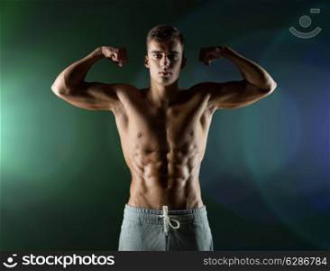sport, bodybuilding, strength and people concept - young man showing biceps and muscles over dark background