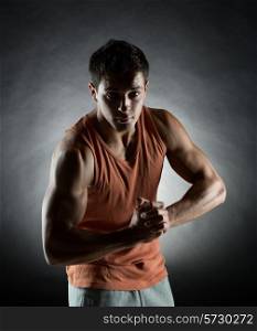 sport, bodybuilding, strength and people concept - young man showing biceps over black background