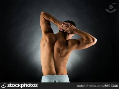 sport, bodybuilding, strength and people concept - young man standing over black background from back