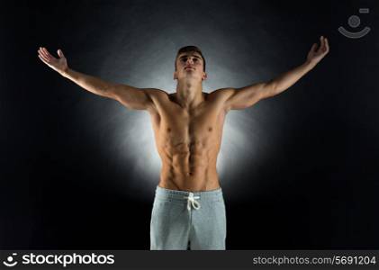 sport, bodybuilding, strength and people concept - young man standing with raised hands over black background