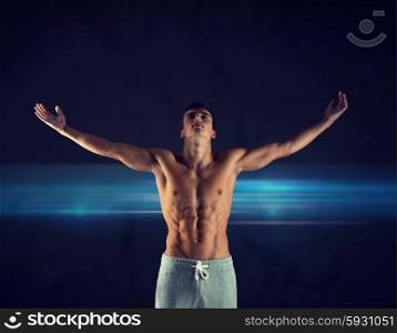 sport, bodybuilding, strength and people concept - young man standing with raised hands over dark background