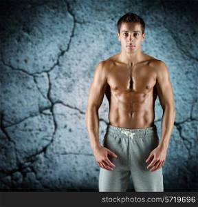 sport, bodybuilding, strength and people concept - young man with bare muscular torso standing over concrete wall background
