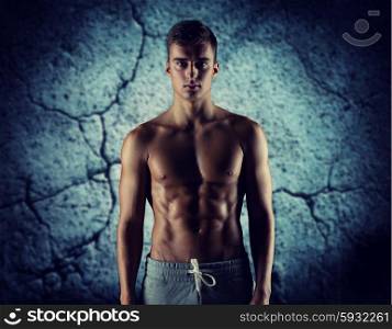 sport, bodybuilding, strength and people concept - young man with bare muscular torso standing over concrete wall background