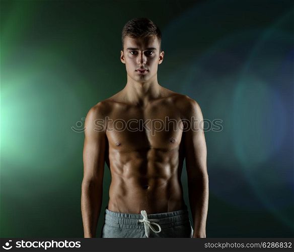 sport, bodybuilding, strength and people concept - young man with bare muscular torso standing over dark background