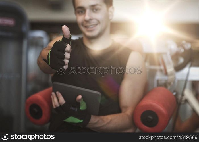 sport, bodybuilding, technology, gesture and people concept - happy young man with tablet pc computer showing thumbs up in gym