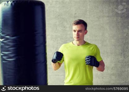 sport, box and people concept - young man in gloves boxing with punching bag in gym