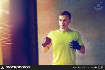 sport, box and people concept - young man in gloves boxing with punching bag in gym. young man in gloves boxing with punching bag