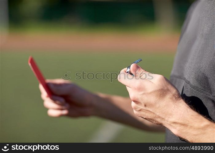 sport, caution, game and people - close up of referee hands with whistle showing red card on football field