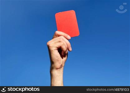 sport, caution, game and people - close up of referee hands with whistle showing red card on football field. referee hands with red card on football field