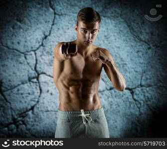 sport, competition, strength and people concept - young man in fighting or boxing position over concrete wall background