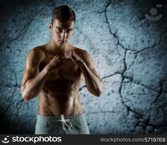 sport, competition, strength and people concept - young man in fighting or boxing position over concrete wall background