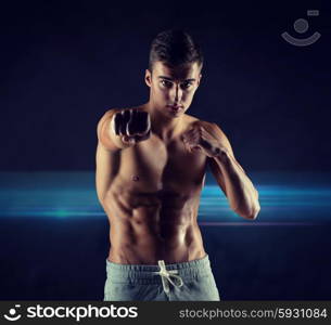 sport, competition, strength and people concept - young man in fighting or boxing position over dark background