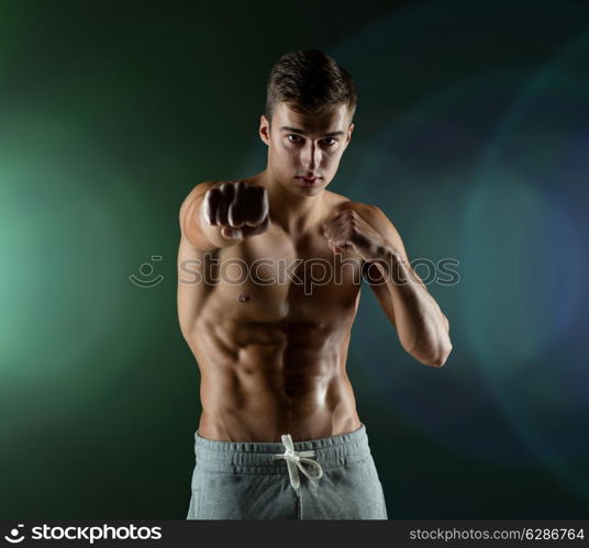 sport, competition, strength and people concept - young man in fighting or boxing position over dark background