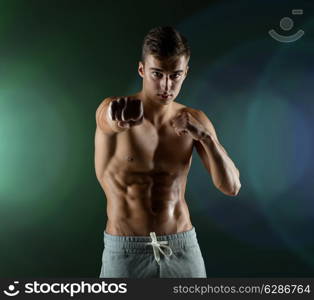 sport, competition, strength and people concept - young man in fighting or boxing position over dark background