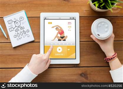 sport, education, technology and people concept - close up of woman with fitness application on tablet pc computer screen, notebook and coffee on wooden table