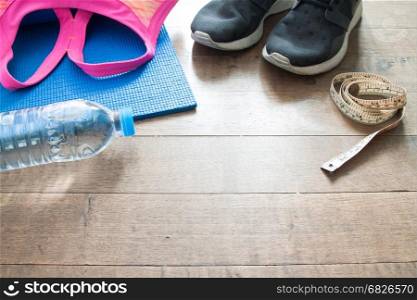 Sport equipments on wooden floor,measuring- tape, sport bra, sneaker and bottle of water and yoga mat
