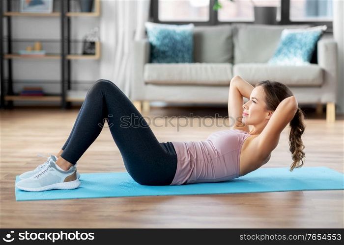 sport, fitness and exercising concept - happy young woman doing sit-ups at home. young woman exercising and doing sit-ups at home