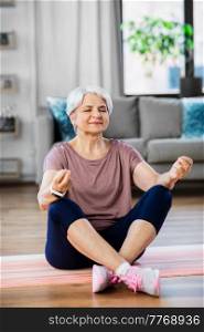 sport, fitness and healthy lifestyle concept - happy senior woman meditating on exercise mat at home. happy senior woman meditating on mat at home
