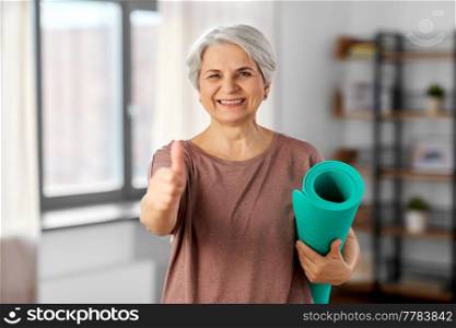 sport, fitness and healthy lifestyle concept - happy smiling senior woman with yoga mat showing thumbs up at home. senior woman with yoga mat showing thumbs up