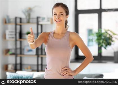sport, fitness and healthy lifestyle concept - happy smiling woman showing thumbs up at home. sporty smiling woman showing thumbs up at home