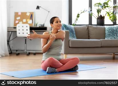 sport, fitness and healthy lifestyle concept - happy smiling young african american woman stretching arm at home. african american woman stretching arm at home