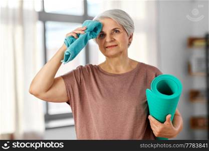 sport, fitness and healthy lifestyle concept - happy tired senior woman with yoga mat and towel at home. happy tired senior woman with yoga mat and towel