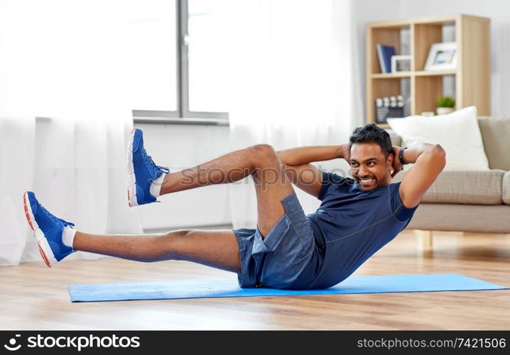 sport, fitness and healthy lifestyle concept - indian man making abdominal exercises at home. indian man making abdominal exercises at home