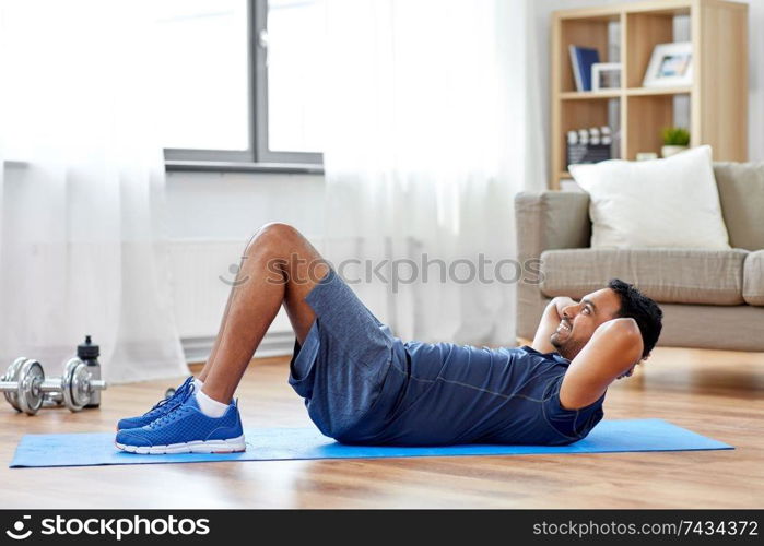 sport, fitness and healthy lifestyle concept - indian man making abdominal exercises at home. indian man making abdominal exercises at home