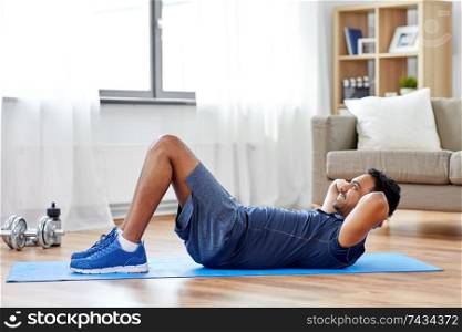sport, fitness and healthy lifestyle concept - indian man making abdominal exercises at home. indian man making abdominal exercises at home