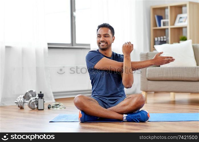 sport, fitness and healthy lifestyle concept - indian man training and stretching arm at home. man training and stretching arm at home