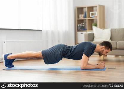 sport, fitness and healthy lifestyle concept - man looking at smartphone and doing plank exercise at home. man doing plank exercise at home