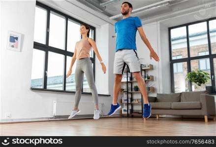 sport, fitness and healthy lifestyle concept - smiling man and woman exercising and jumping at home. happy couple exercising and jumping at home