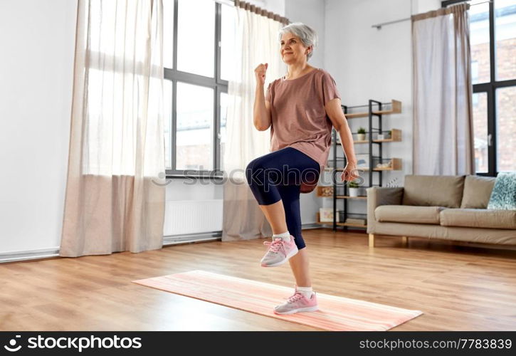 sport, fitness and healthy lifestyle concept - smiling senior woman exercising on mat and walking on spot at home. smiling senior woman exercising on mat at home
