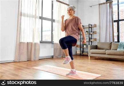 sport, fitness and healthy lifestyle concept - smiling senior woman exercising on mat and walking on spot at home. smiling senior woman exercising on mat at home