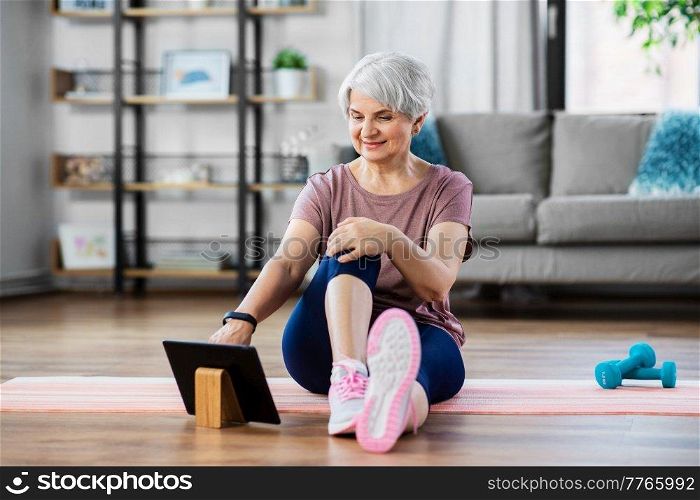 sport, fitness and healthy lifestyle concept - smiling senior woman exercising with tablet pc computer on mat at home. happy woman with tablet pc exercising at home