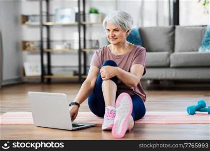 sport, fitness and healthy lifestyle concept - smiling senior woman exercising with laptop computer on mat at home. happy woman with laptop exercising at home