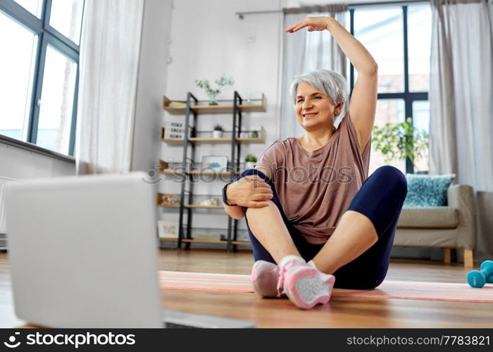 sport, fitness and healthy lifestyle concept - smiling senior woman exercising with laptop computer on mat at home. happy woman with laptop exercising at home