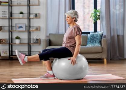 sport, fitness and healthy lifestyle concept - smiling senior woman training by sitting on exercise ball at home. senior woman training with exercise ball at home