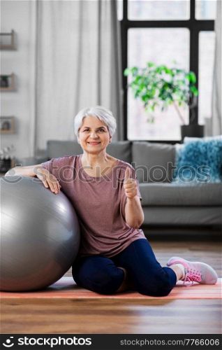 sport, fitness and healthy lifestyle concept - smiling senior woman with exercise ball showing thumbs up sitting on mat at home. smiling senior woman with exercise ball at home