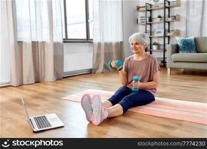 sport, fitness and healthy lifestyle concept - smiling senior woman with laptop computer and dumbbells exercising on mat at home. woman with laptop and dumbbells exercising at home
