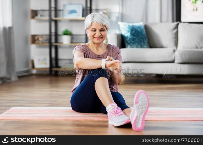 sport, fitness and healthy lifestyle concept - smiling senior woman with smart watch or tracker exercising at home. smiling senior woman with fitness tracker at home