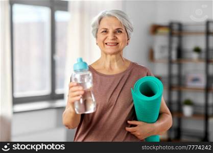 sport, fitness and healthy lifestyle concept - smiling senior woman with yoga mat and bottle of water at home. senior woman with yoga mat and bottle of water
