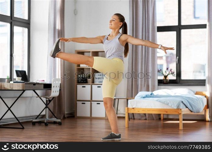 sport, fitness and healthy lifestyle concept - smiling teenage girl exercising and stretching leg at home. happy teenage girl exercising at home