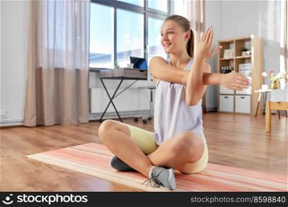 sport, fitness and healthy lifestyle concept - smiling teenage girl exercising on yoga mat and stretching hand at home. happy teenage girl exercising on yoga mat at home